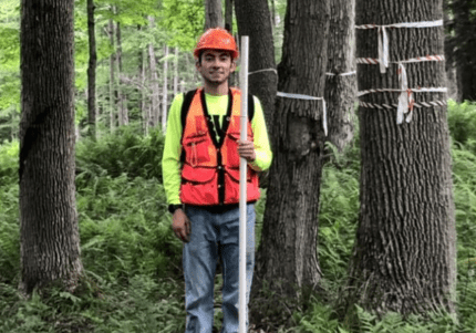 Brandon Marcucci '21站在阿勒格尼国家森林的树木中，用齿轮测量树木.